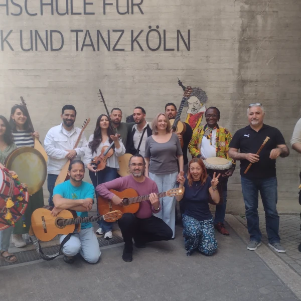Eine Gruppe von Absolvent:innen des Zertifikatslehrgangs steht mit unterschiedlichsten Instrumenten vor der Hochschule für Musik und Tanz Köln